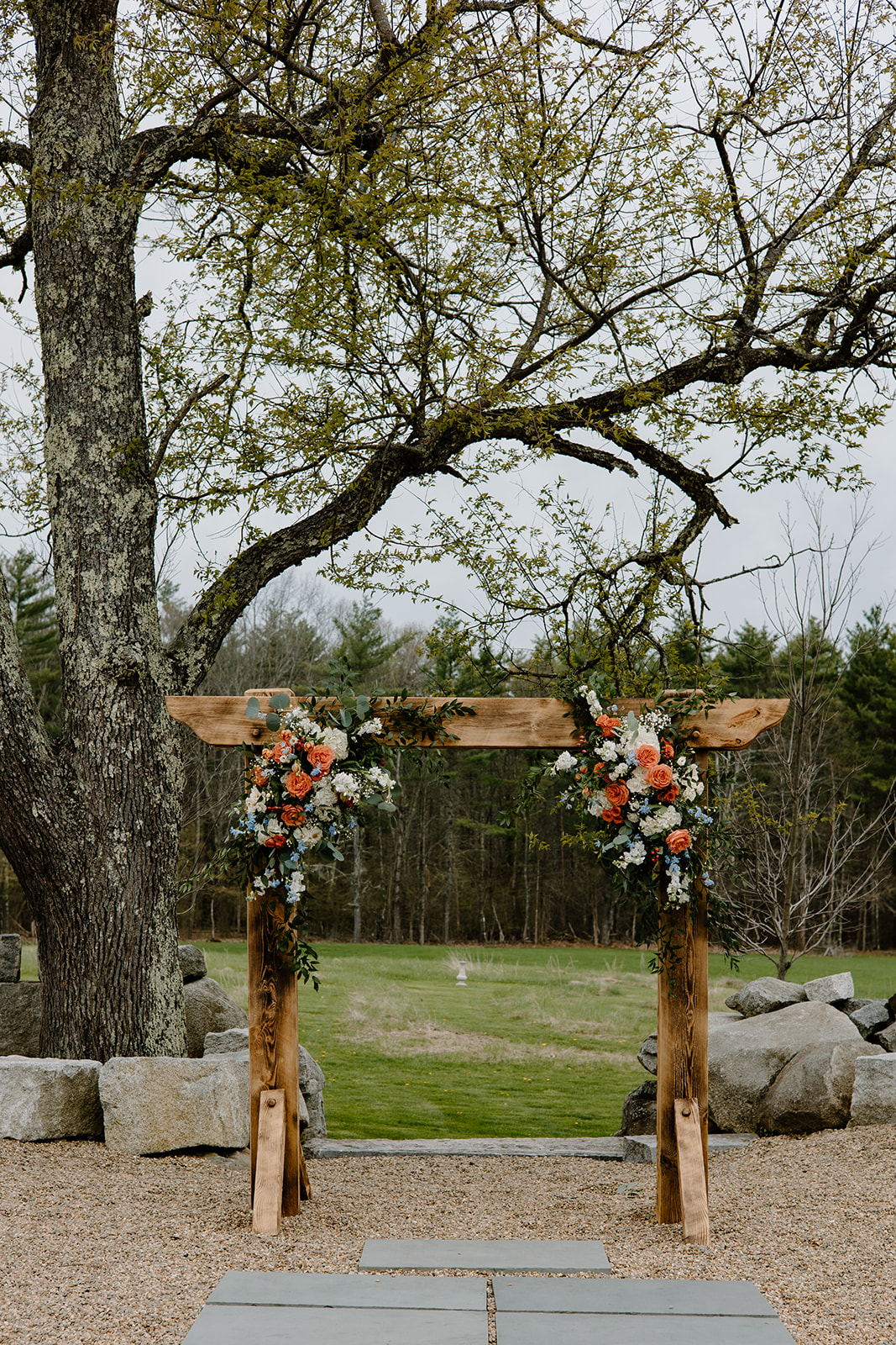 Rustic wedding arch with orange and blue flowers.
