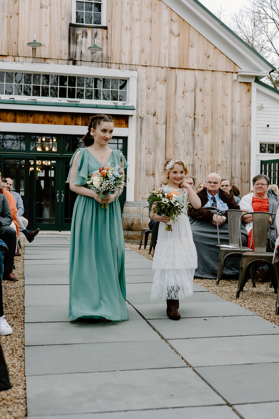 Maid of honor wearing a blue dress and young flower girl walking down the aisle outside Powder Major's Barn in Madbury, New Hampshire.