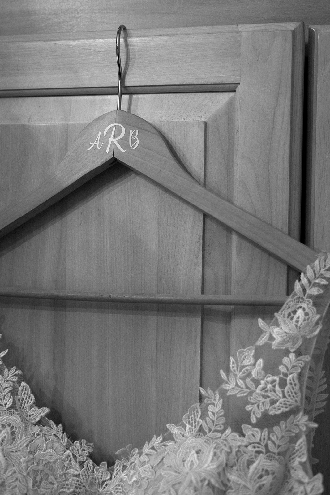 Black and white detail photo of a lace wedding gown hanging on a custom wooden hanger.