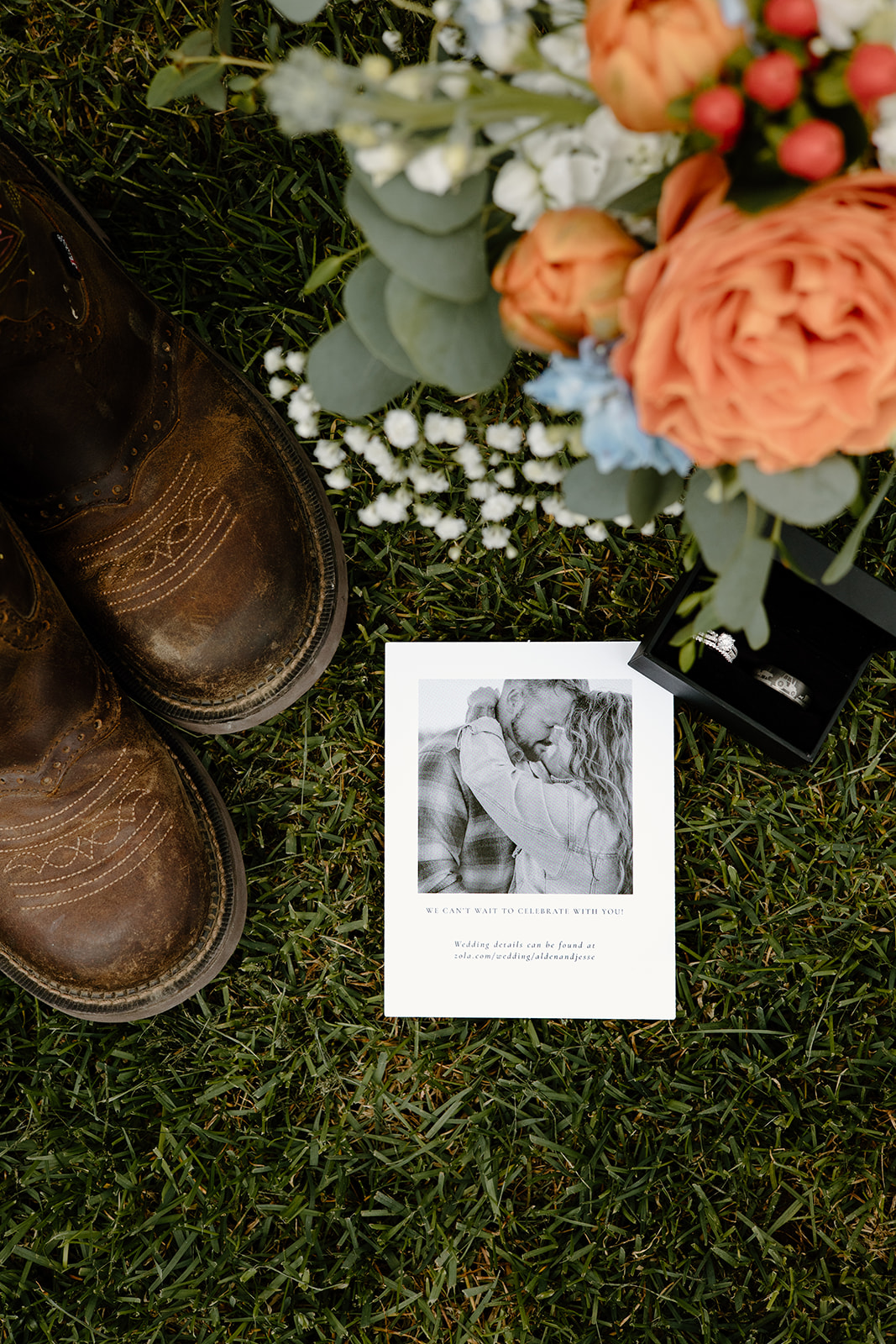 Rustic wedding detail flat lay with boots, a orange and blue bridal bouquet and the couple's wedding invitation.