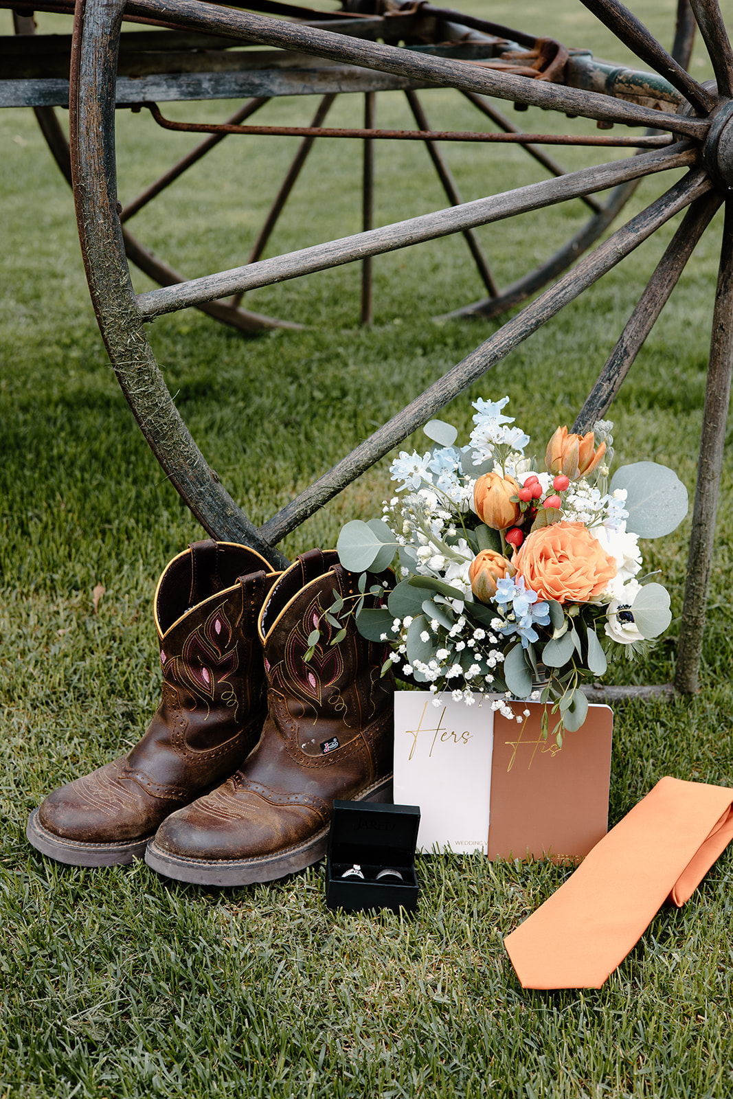 Rustic wedding detail flat lay with vow books, rings, bouquet and the bride's boots.