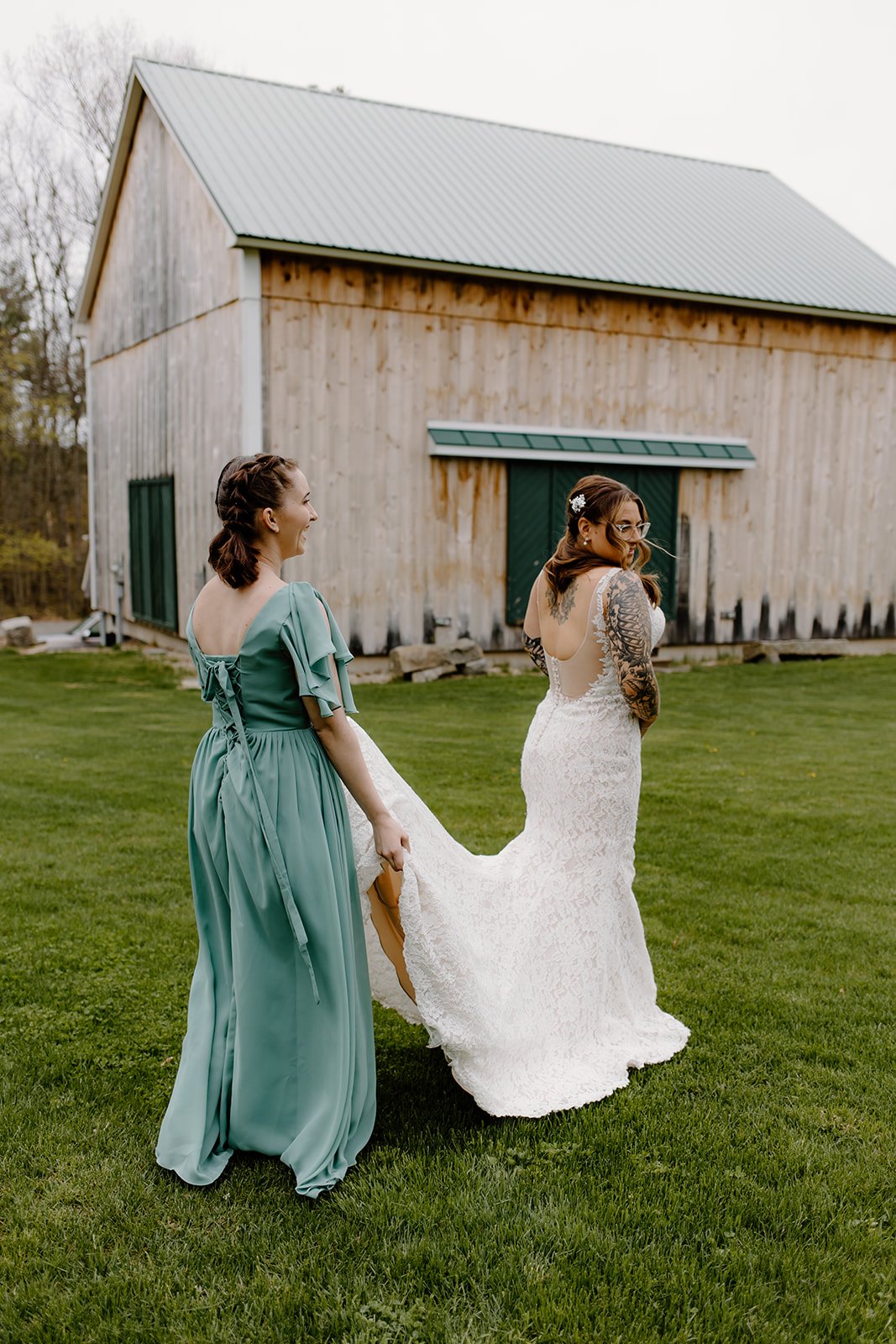 Bridesmaid holding bride's dress train outside of The Barn at Powder Major's Farm in New Hampshire.