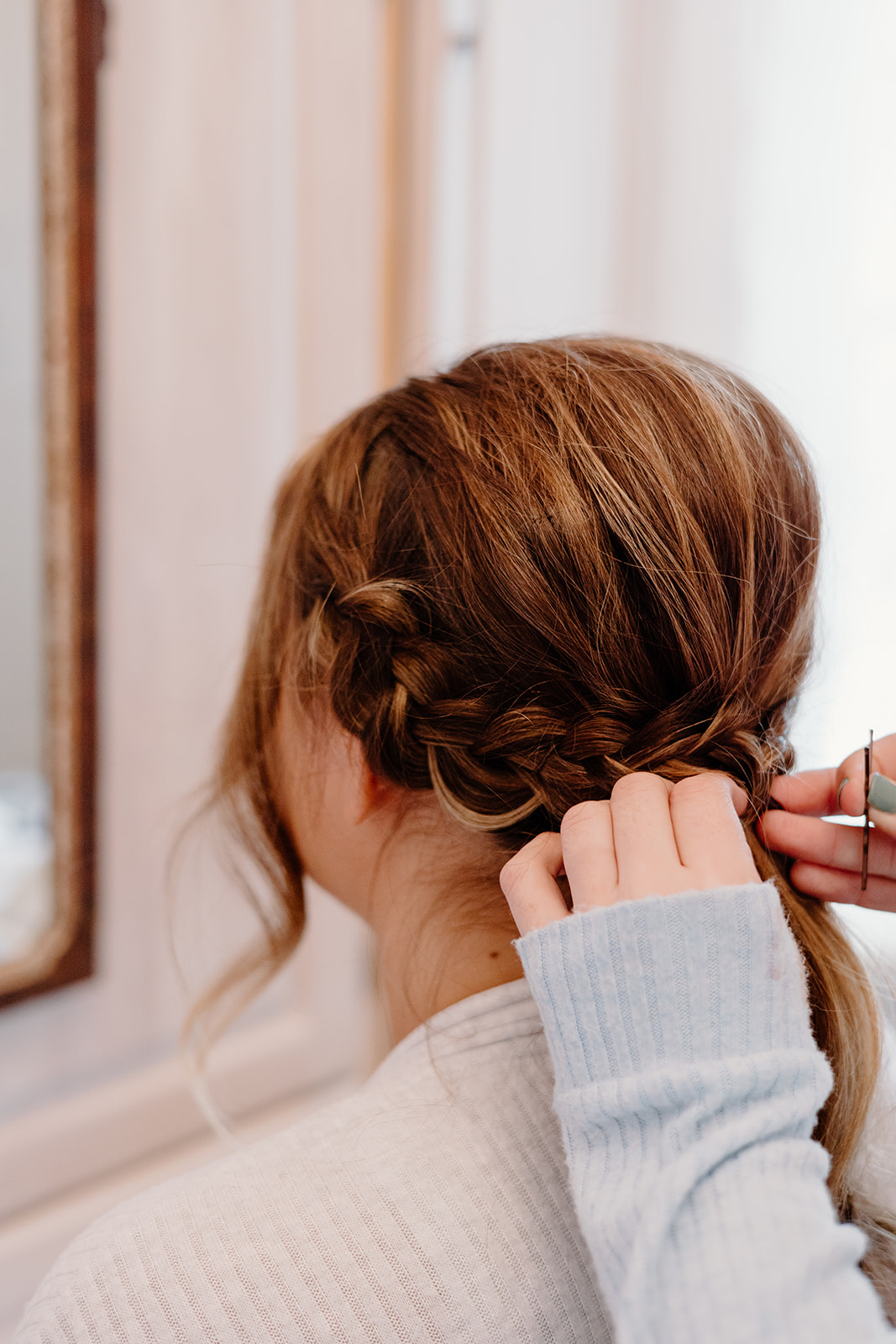 A bride getting her hair done into a braided low-ponytail.