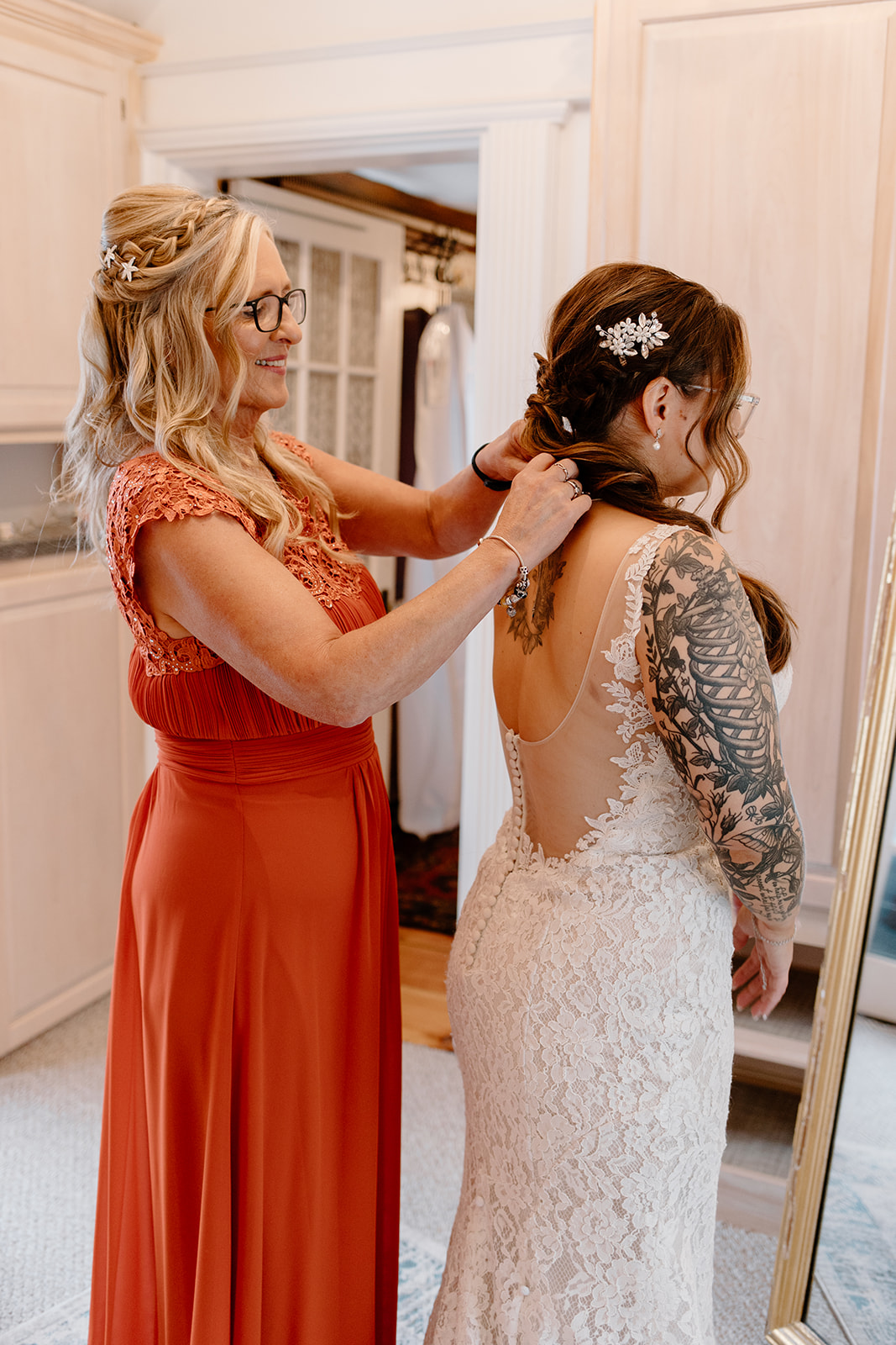 Mother-of-the-bride wearing an orange dress helping the bride get ready.