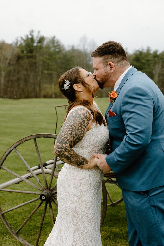 Bride and groom kissing in front of a vintage wagon.