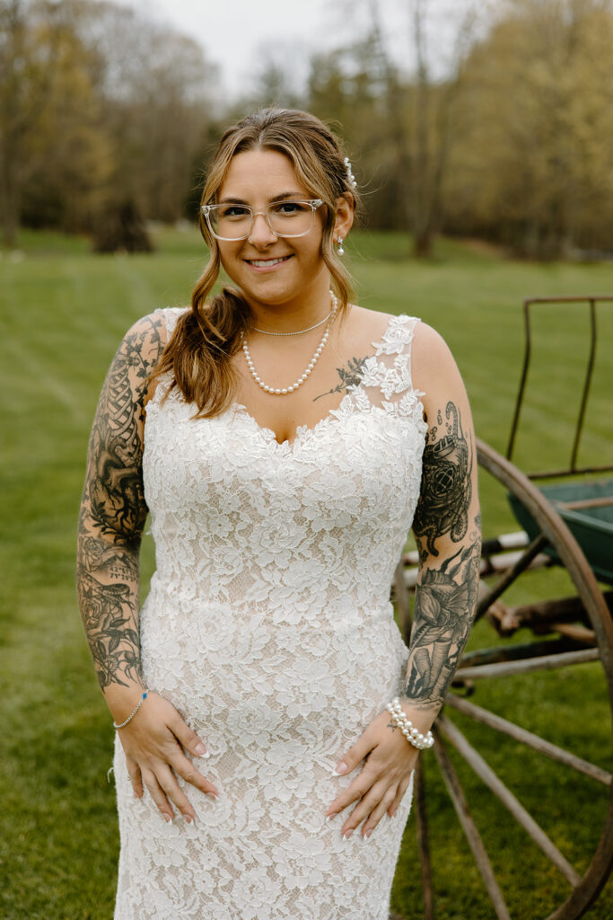Bride with sleeve tattoos wearing a fitted lace dress and pearl necklace posing in front of a vintage wagon.