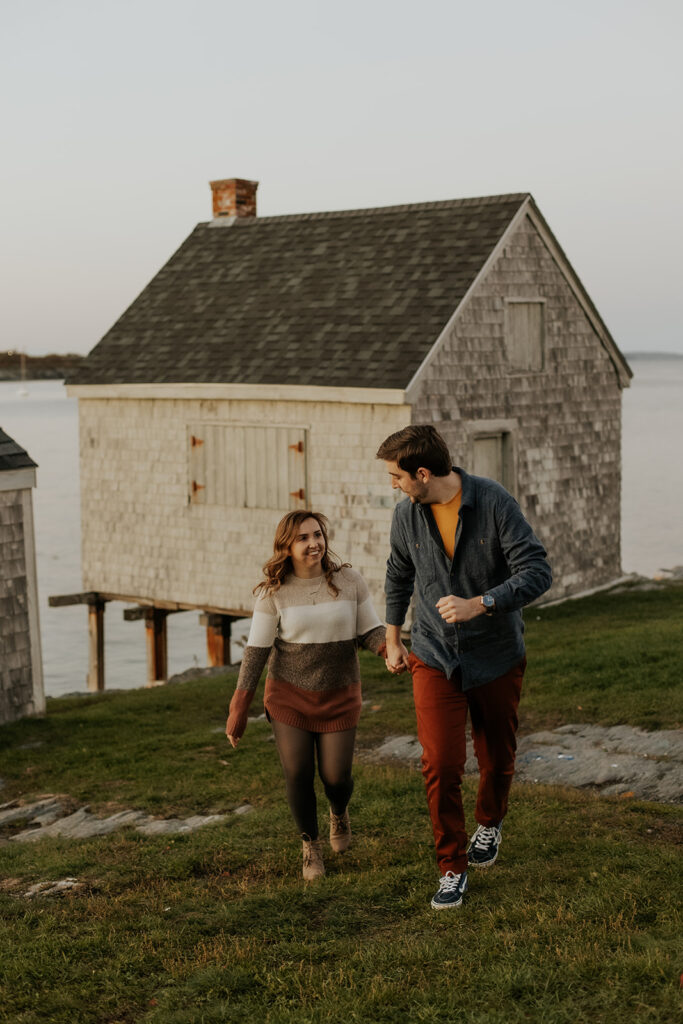 Couple walking at Fisherman's Point in Portland, Maine with a weathered structure in the background.