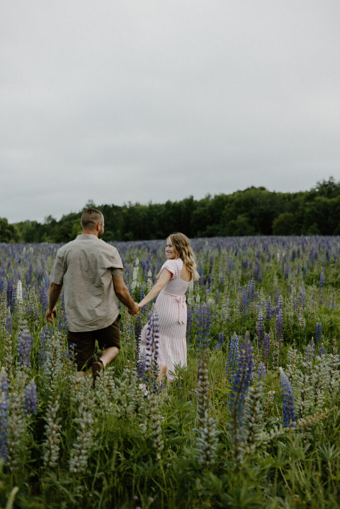 Couple walking through the Wild Lupine Fields in Maine for their romantic, whimsical engagement session.