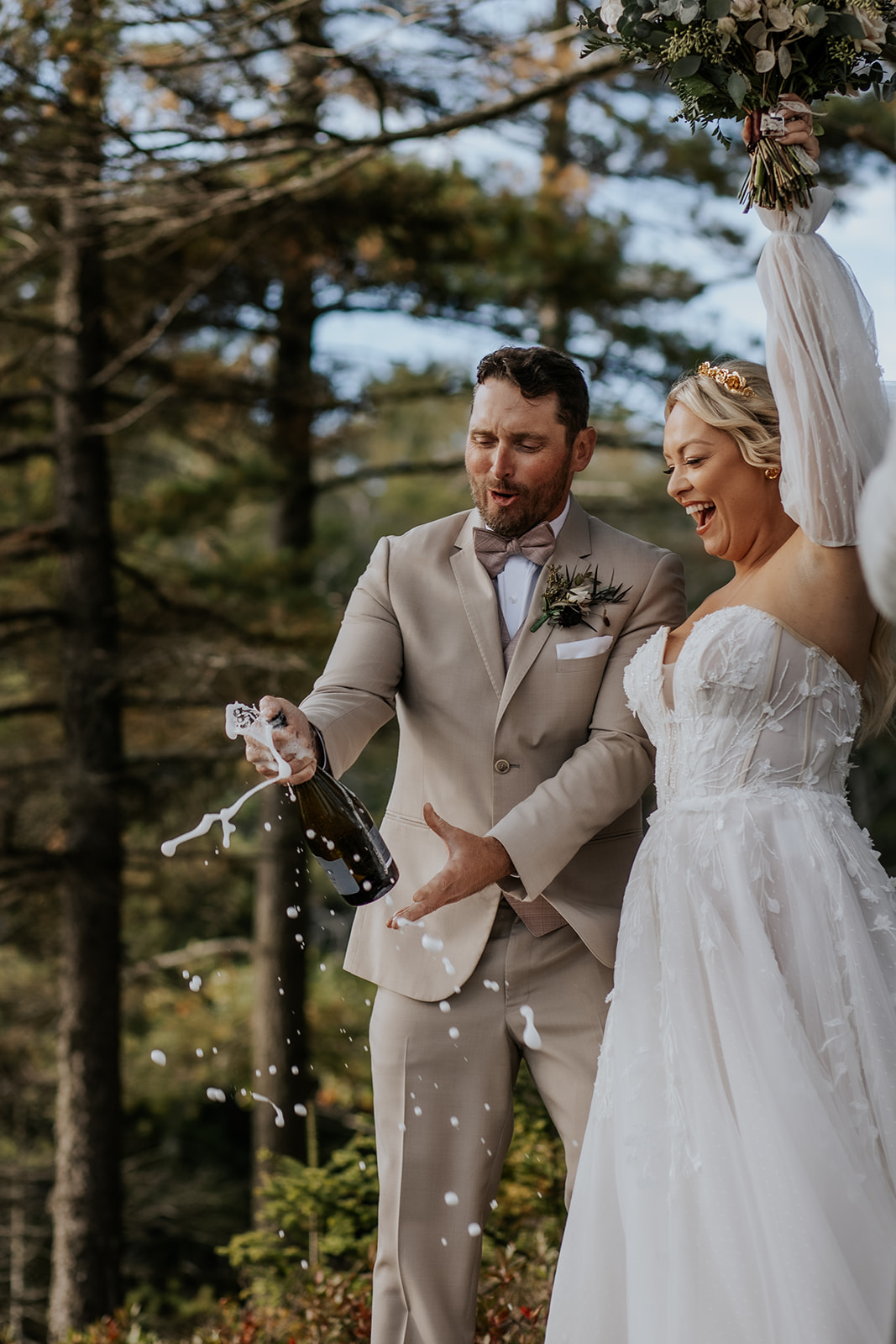 Bride and groom champagne pop against a forest backdrop in Maine.