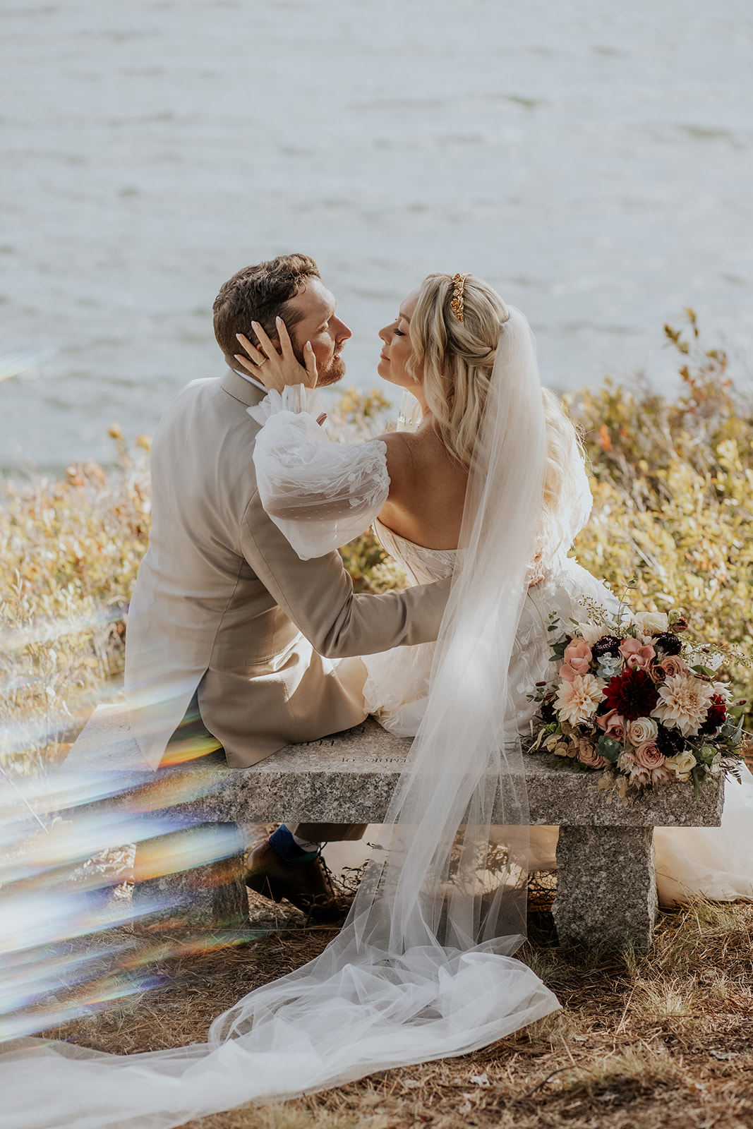 Bride and groom sitting on a bench overlooking the ocean in coastal Maine.