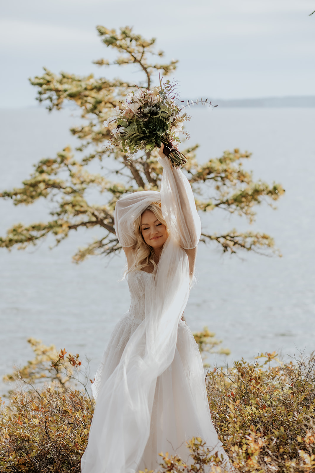 Bride holding up her bouquet with the Maine coast in the background.