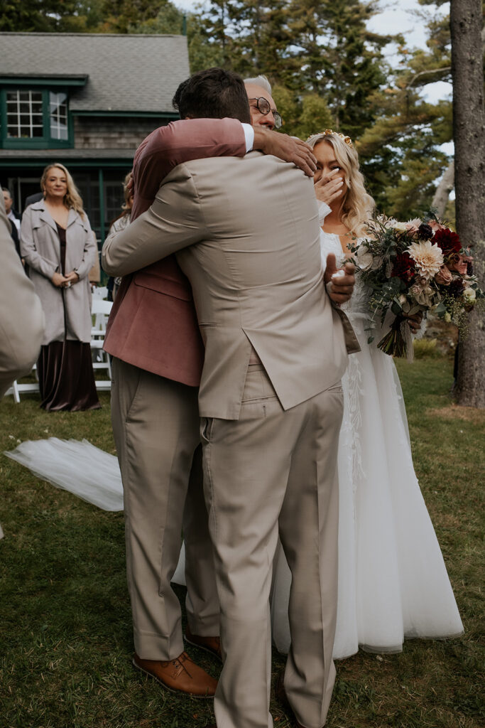 Wedding ceremony groom and bride's father hugging.