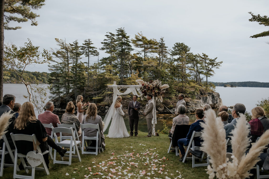Outdoor fall wedding ceremony in Bath, Maine with the ocean and pine trees in the background.