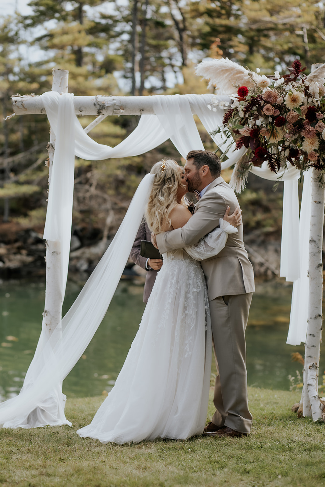 Bride and groom first kiss under a birch wood arbor with drapery and florals.