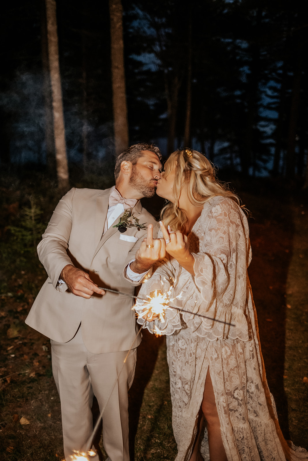 Bride and groom flipping off the camera with their ring fingers and holding sparklers.