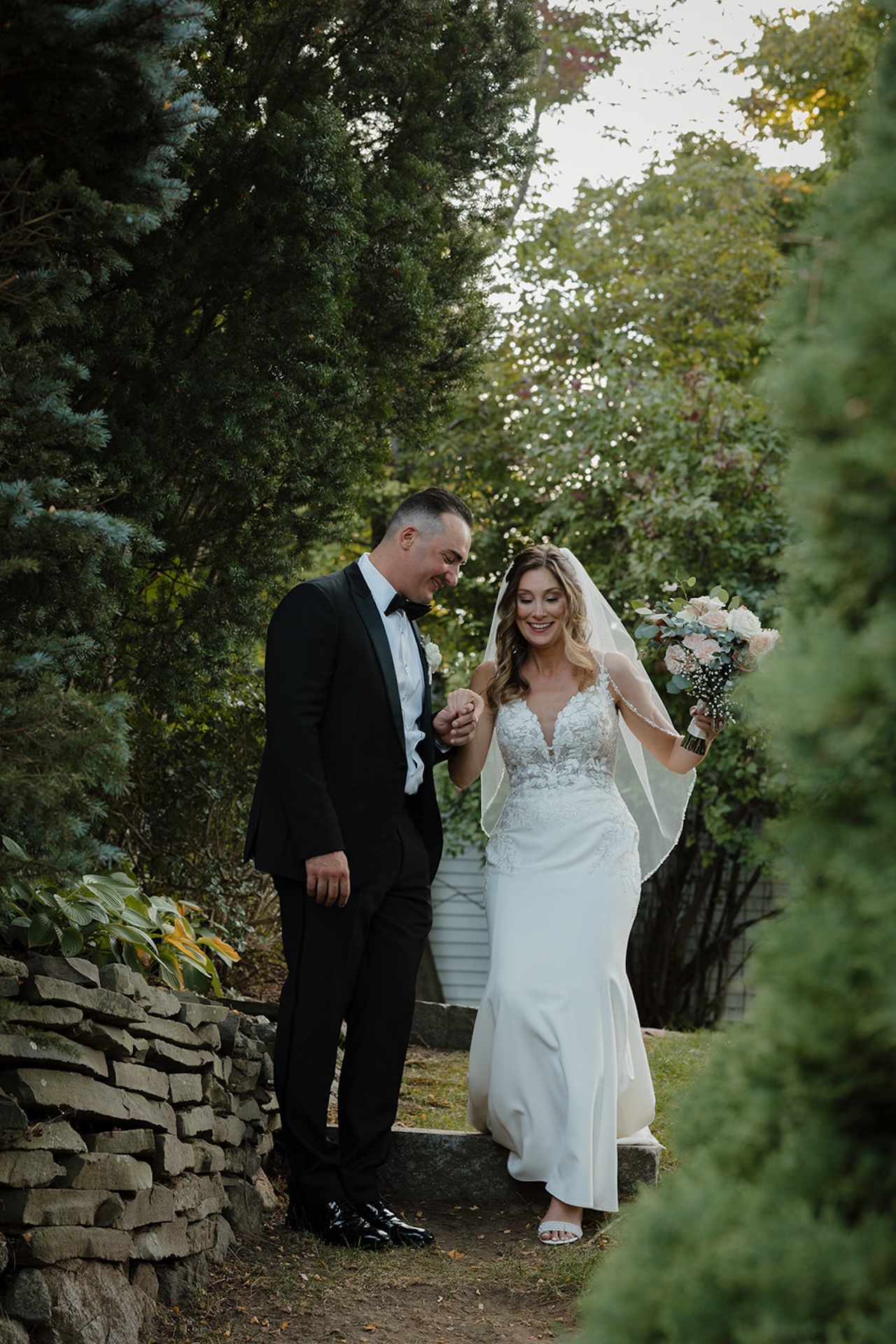 Bride and groom walking through a garden pathway, he gently holds her hand as she carries a bouquet, a natural and candid moment tied to Destination Wedding Location Ideas.