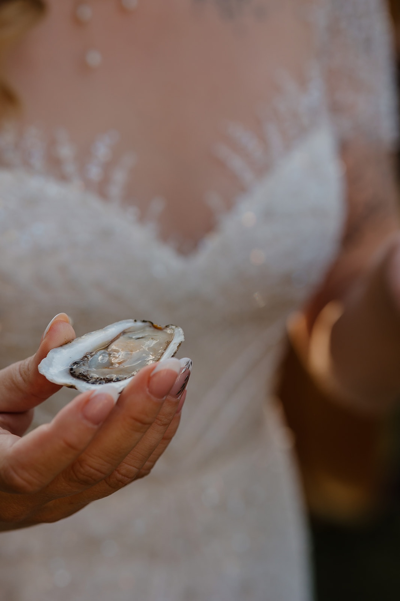 Close-up of a bride holding a fresh oyster in her hand, a nod to coastal wedding traditions and Destination Wedding Location Ideas.