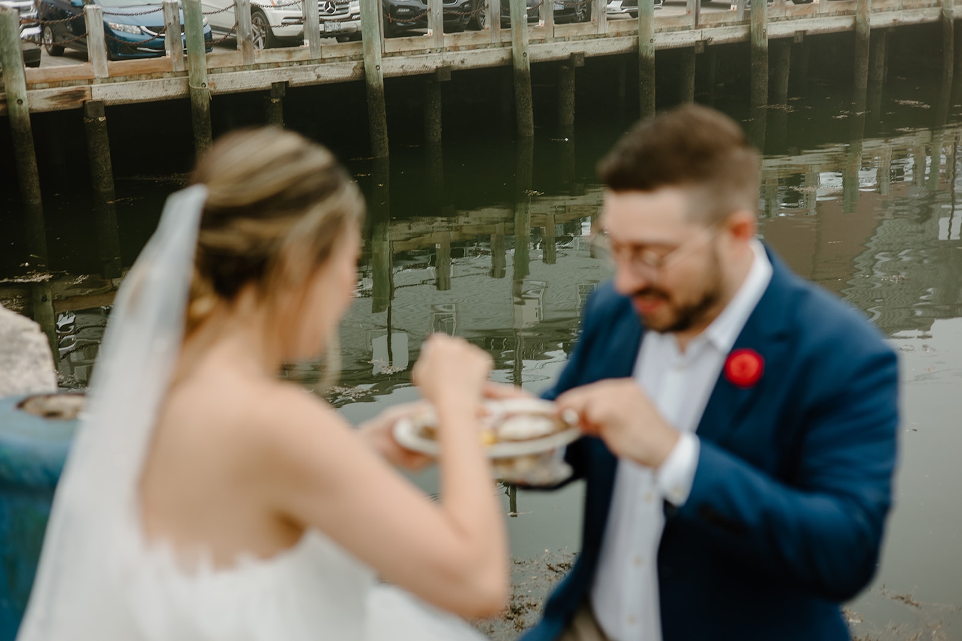 Bride and groom laughing together while eating oysters by the dock, candid wedding day fun.