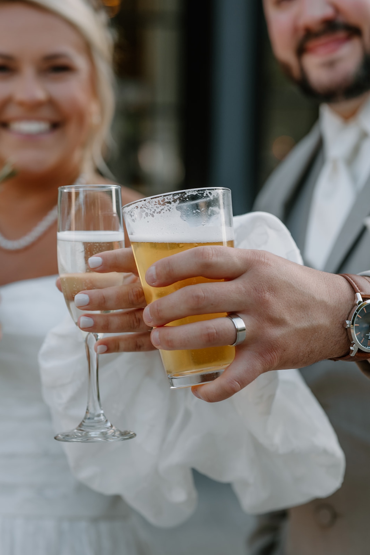 Close-up of bride and groom clinking glasses of champagne and beer during cocktail hour, a fun detail moment reflecting Destination Wedding Location Ideas.