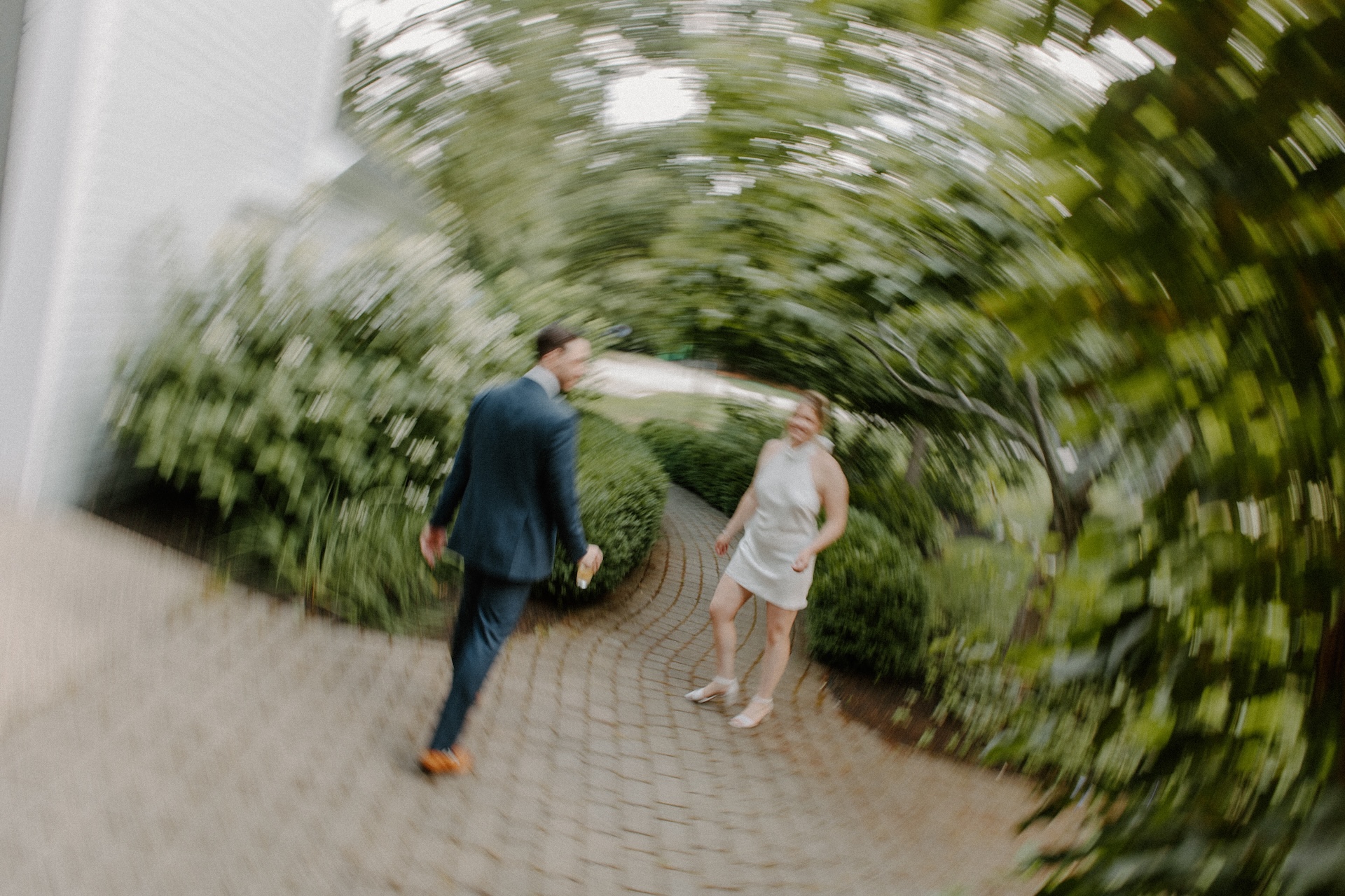 A creative blurred motion shot of the bride and groom walking down a cobblestone path, surrounded by lush greenery.
