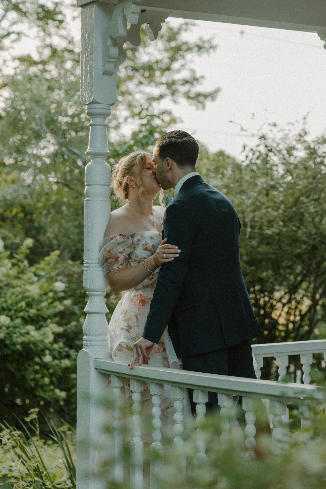 The bride and groom sharing a kiss on the wraparound porch of the farmhouse at a Portland Maine wedding venue.