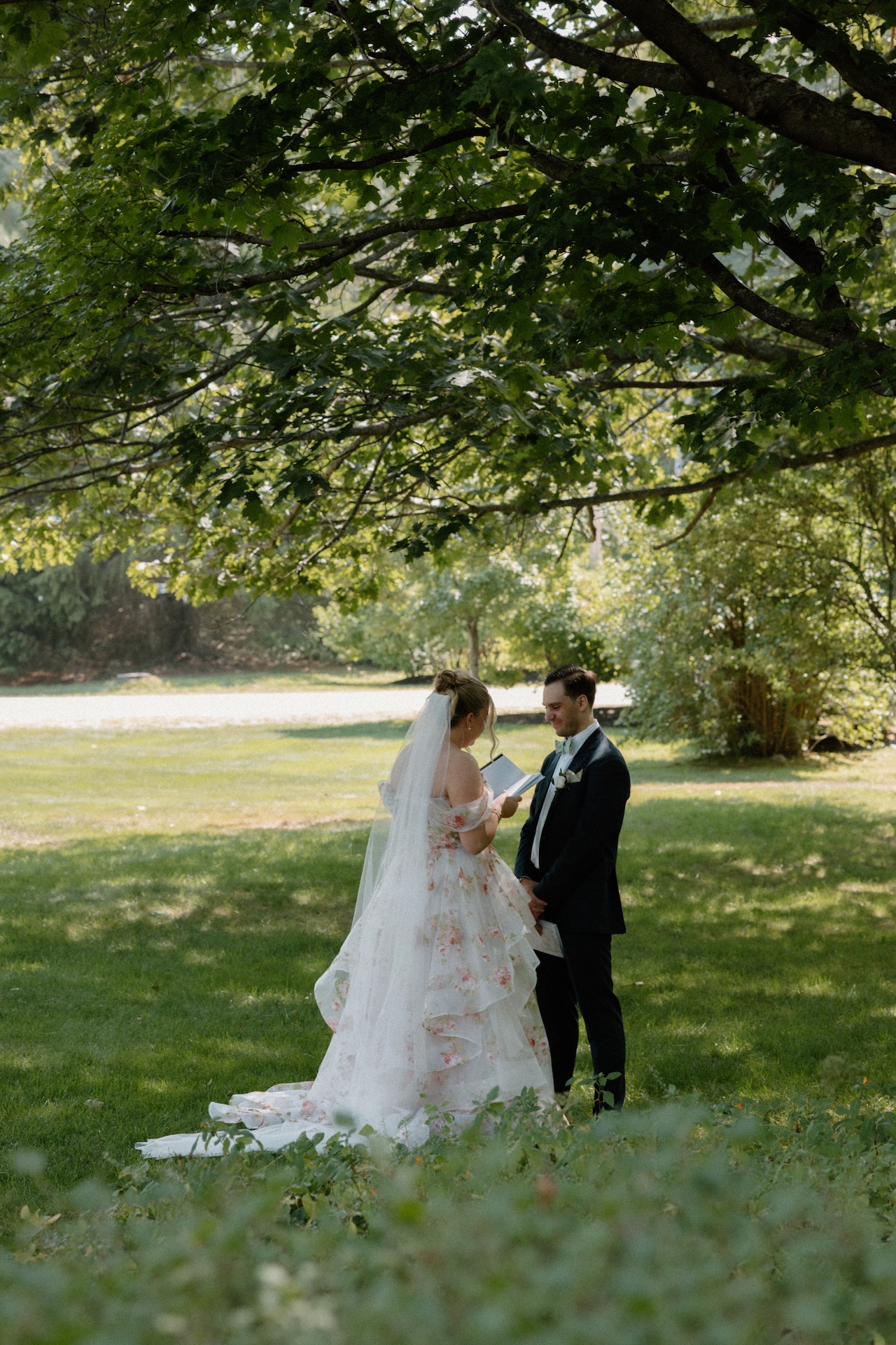 The bride reading her vows to the groom in the garden, standing in front of a historic farmhouse at a Portland Maine wedding venue.