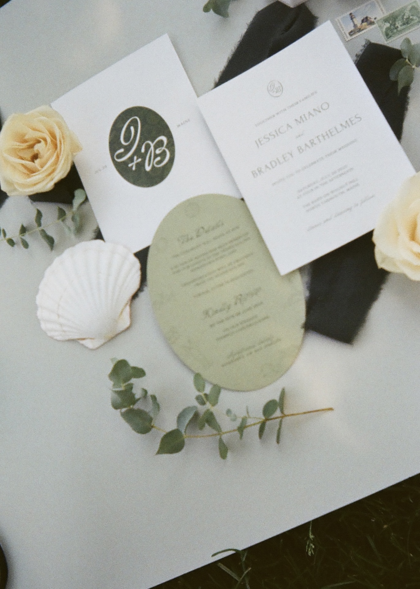 Flat lay of wedding invitations, programs, and a seashell detail styled with yellow roses and greenery.