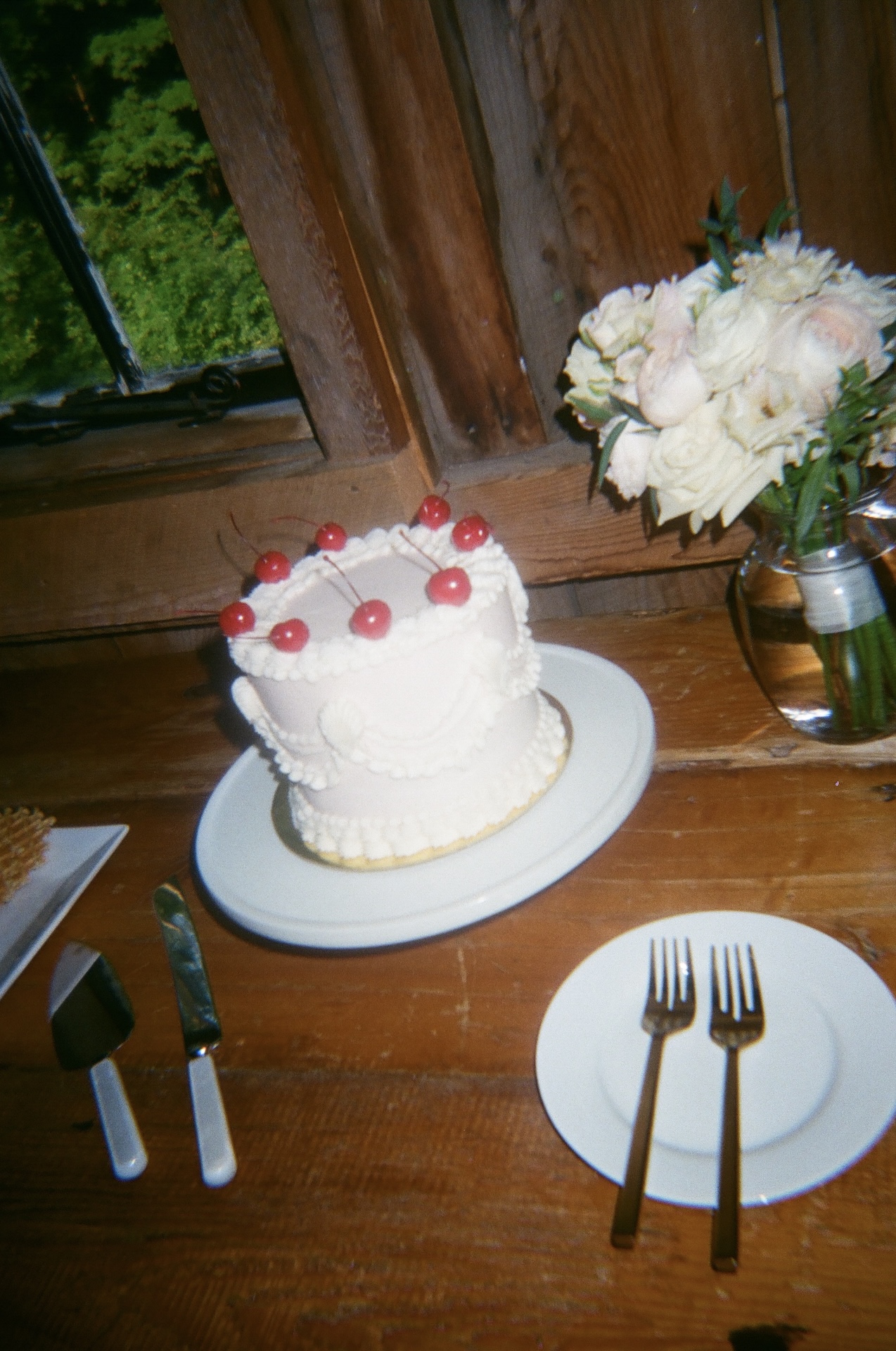 A vintage-inspired white cake with cherries on top, displayed beside a vase of flowers at a Portland Maine wedding venue.