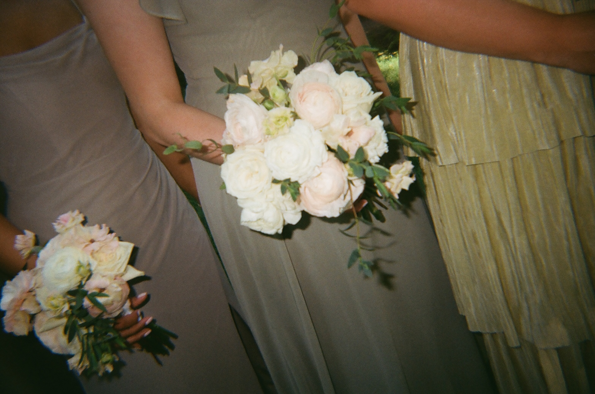 Close-up of bridesmaids holding bouquets of cream and blush roses with soft greenery.