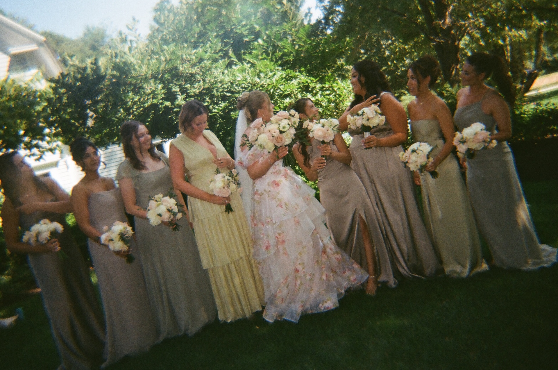 The bride laughing with her bridesmaids, all holding bouquets and wearing soft neutral gowns.