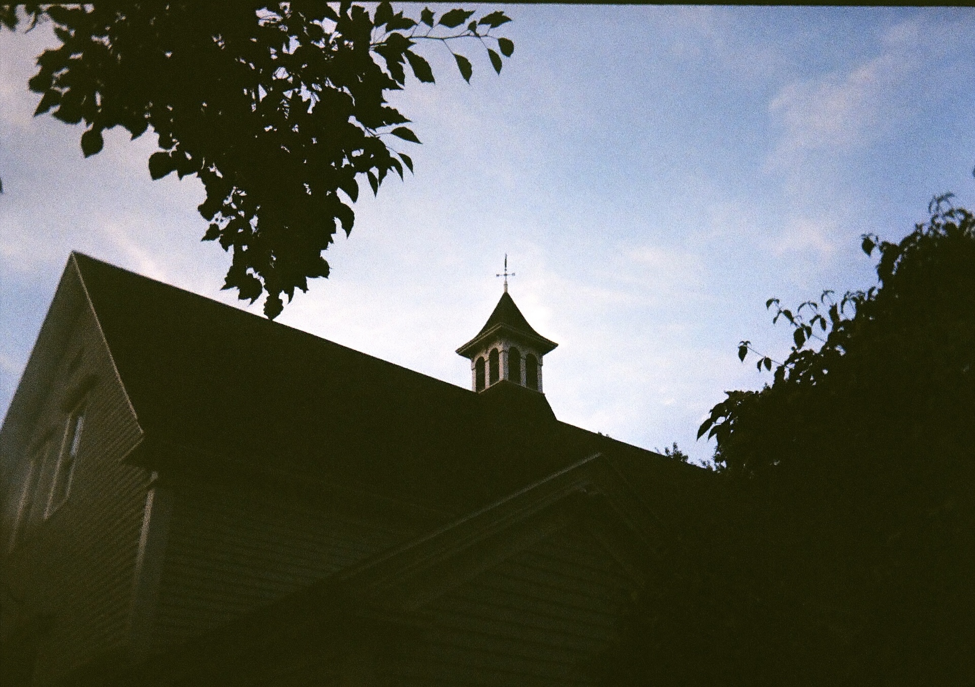 A silhouette view of the historic barn cupola at dusk, framed by tree branches against the evening sky.