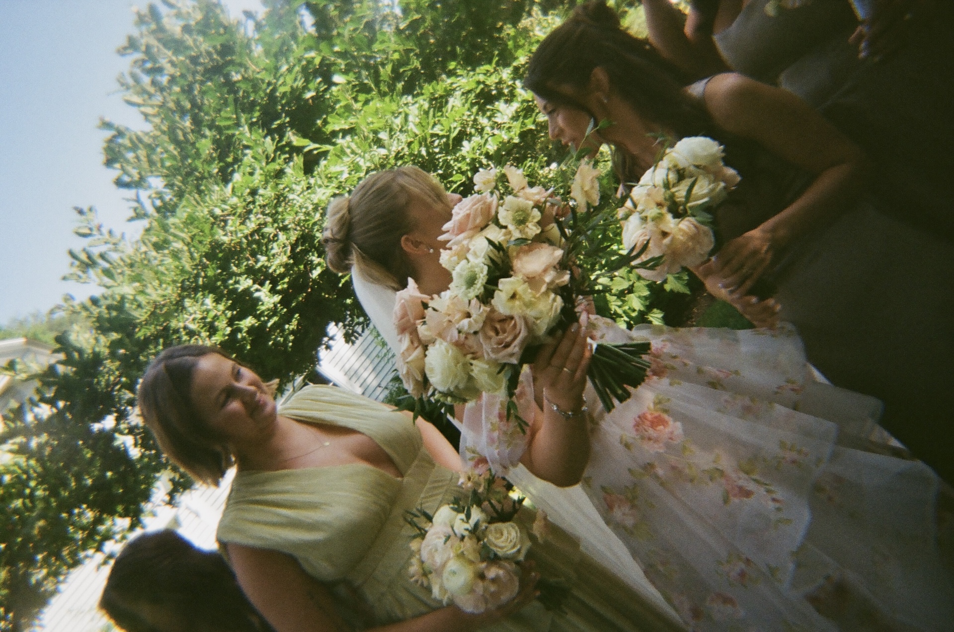 The bride laughing with her bridesmaids outside, holding bouquets of blush and cream roses at a Portland Maine wedding venue.