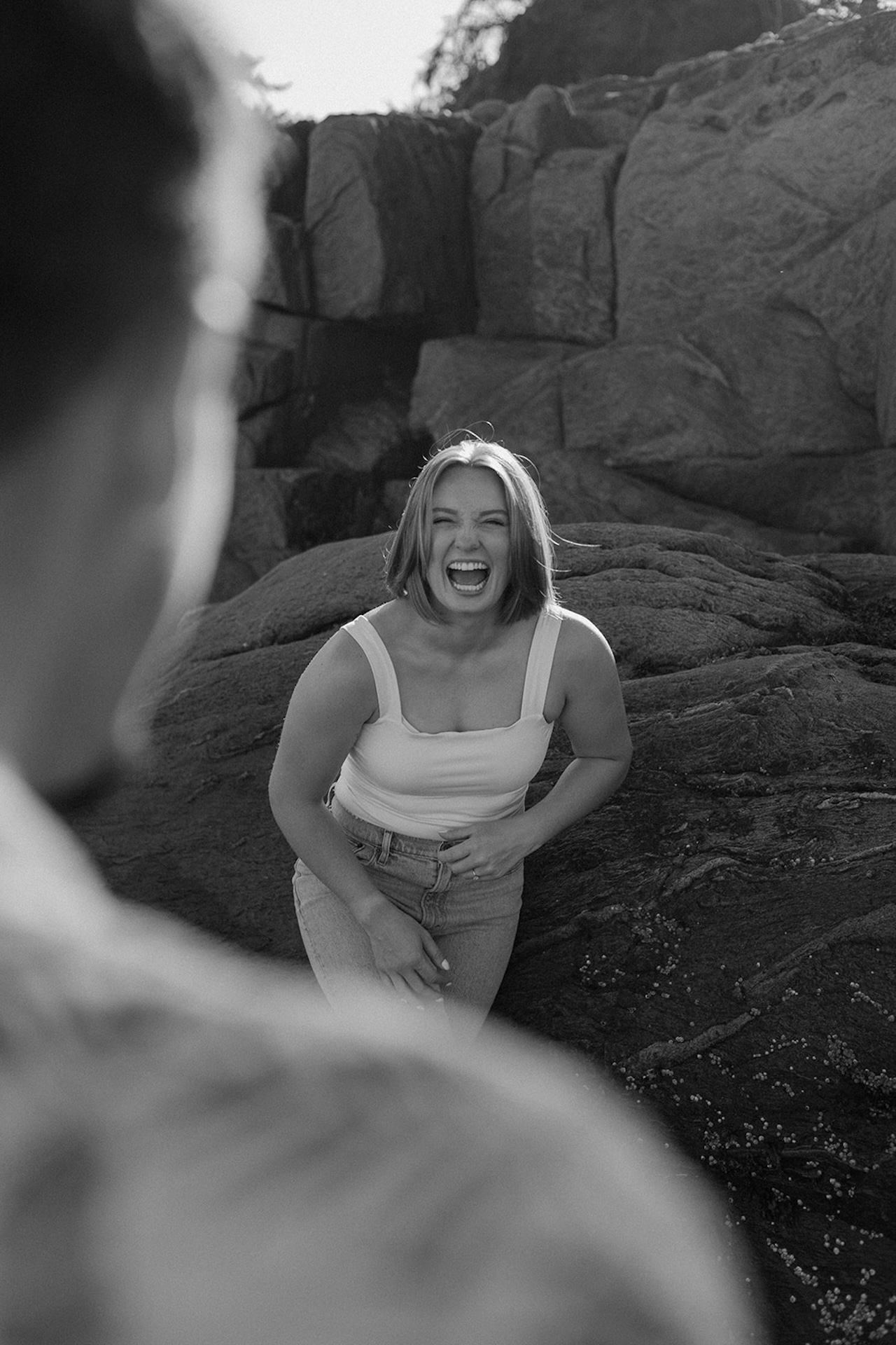 Couple laughing together near seaside rocks, playful energy at one of the prettiest coastal Engagement Photo Locations in Maine.