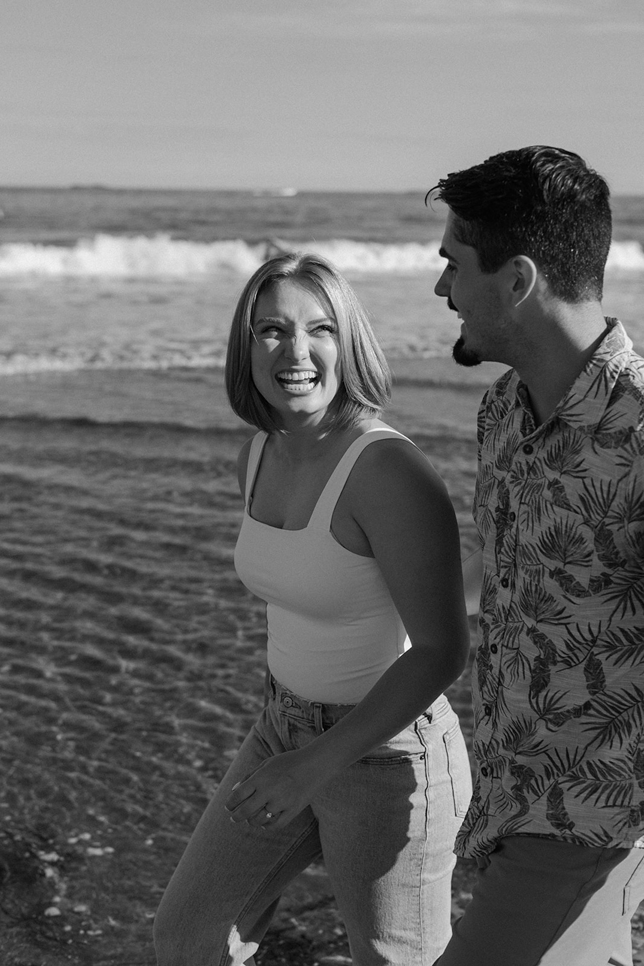 Woman laughing toward her partner while standing near rocky cliffs, natural and carefree Engagement Photo Locations style portrait.