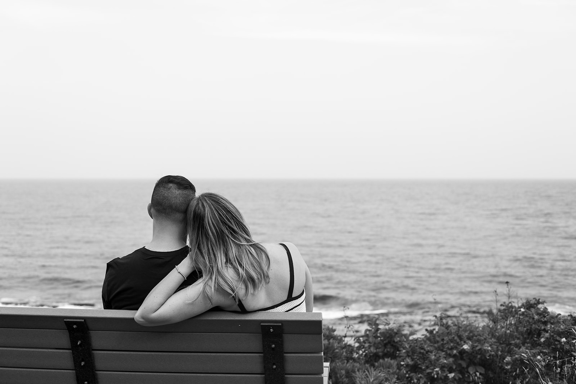 Couple sitting on a seaside bench, gazing out at the ocean horizon together.