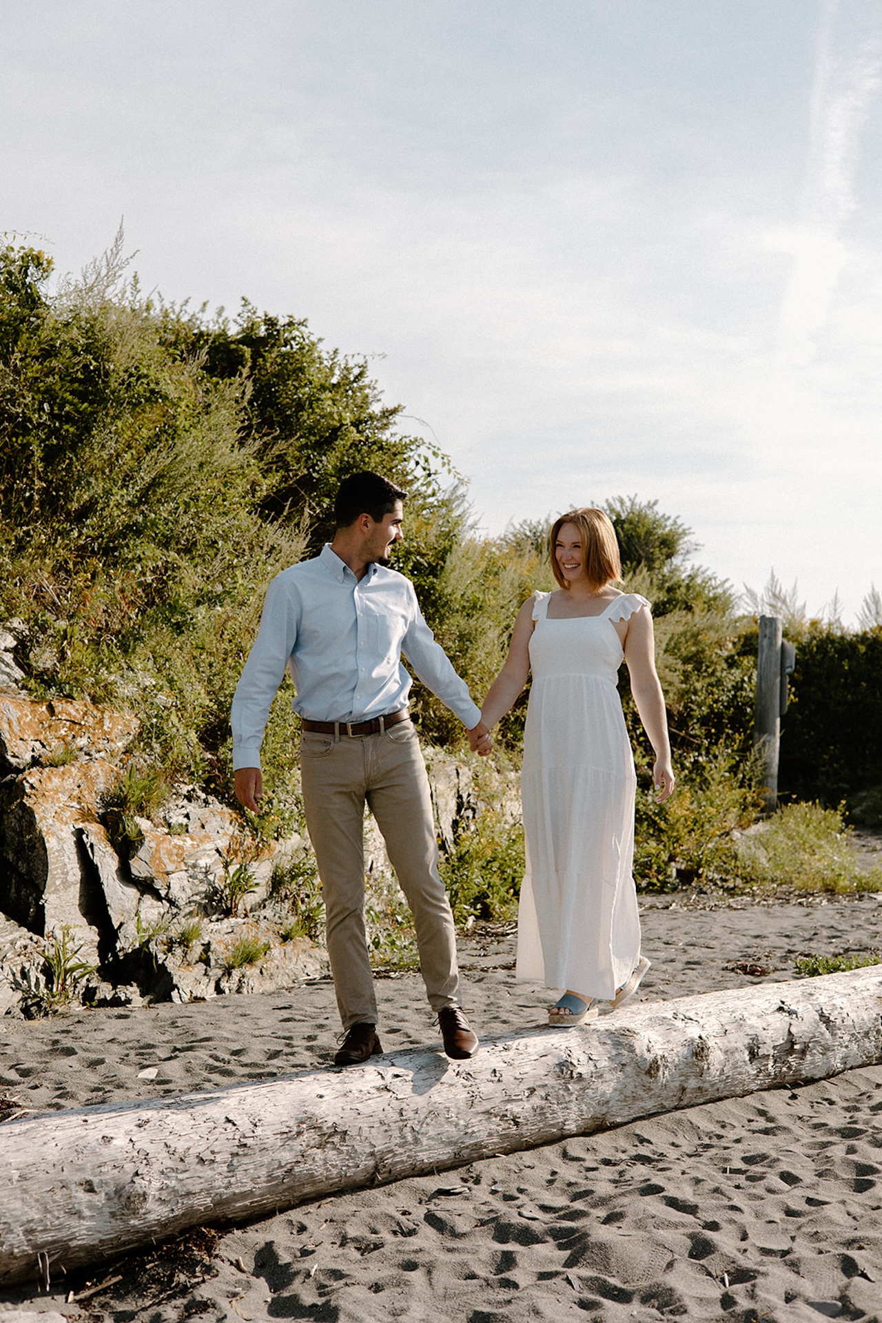 Couple walking hand in hand along a sandy beach path, sunlight highlighting their relaxed connection at one of the prettiest Engagement Photo Locations near Portland.