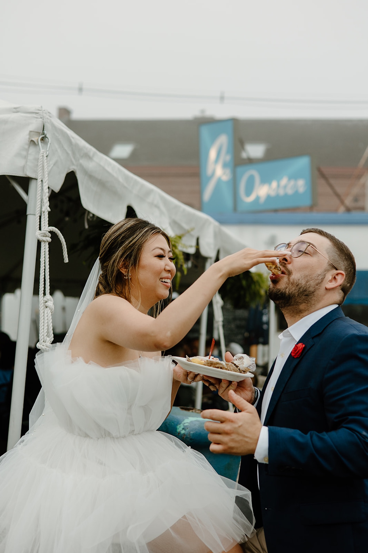 Bride feeding the groom oysters and laughing outside a local seafood restaurant at charming Engagement Photo Locations.