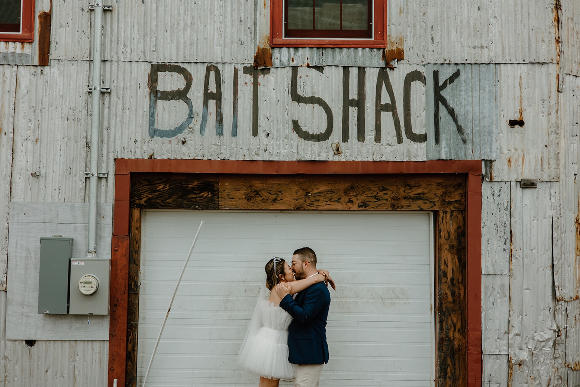 Bride and groom sharing a kiss in front of a rustic building with a “Bait Shack” sign.