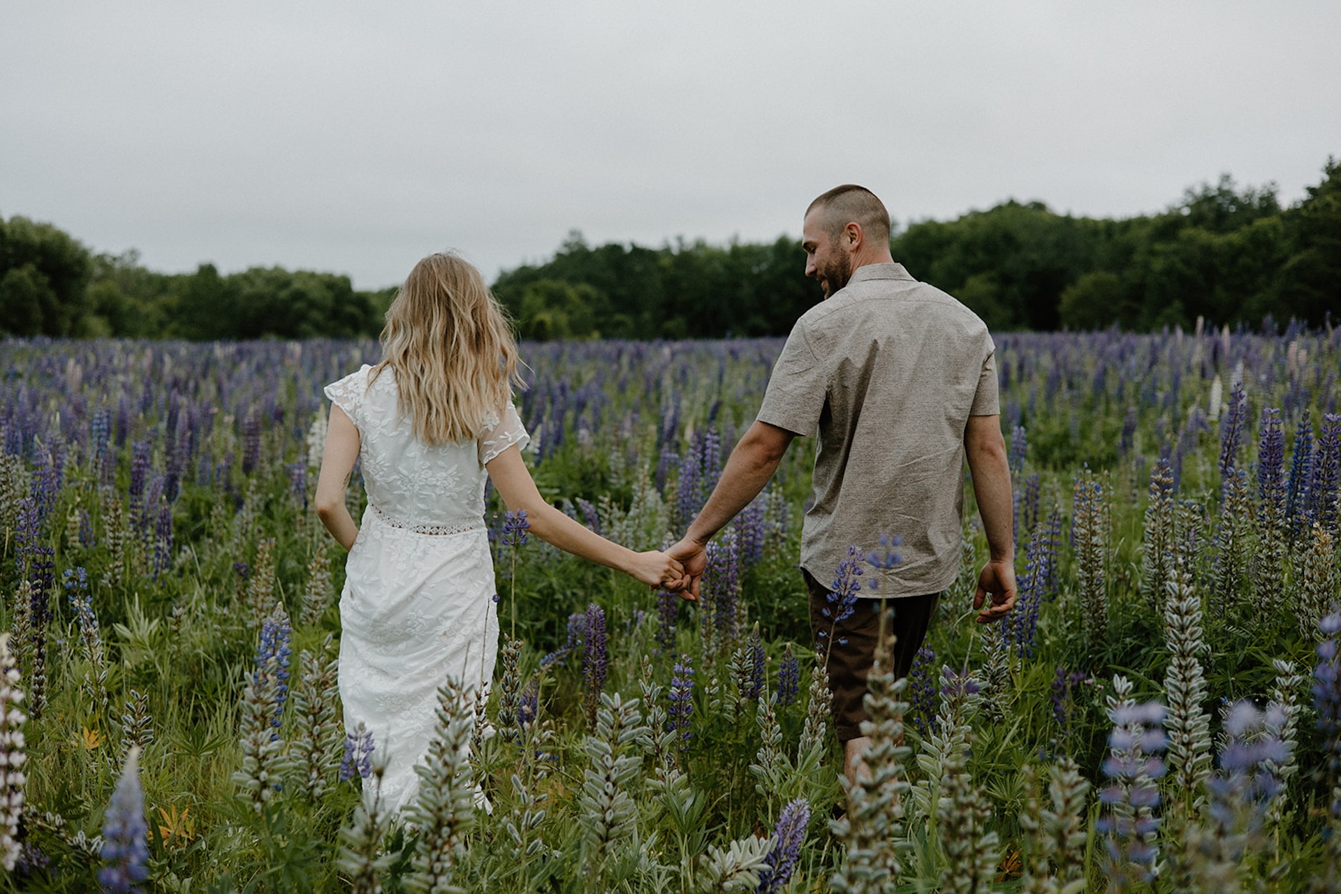 Couple walking hand in hand through a blooming lupine field, blending romance and nature for spring engagement photo locations near Portland Maine.