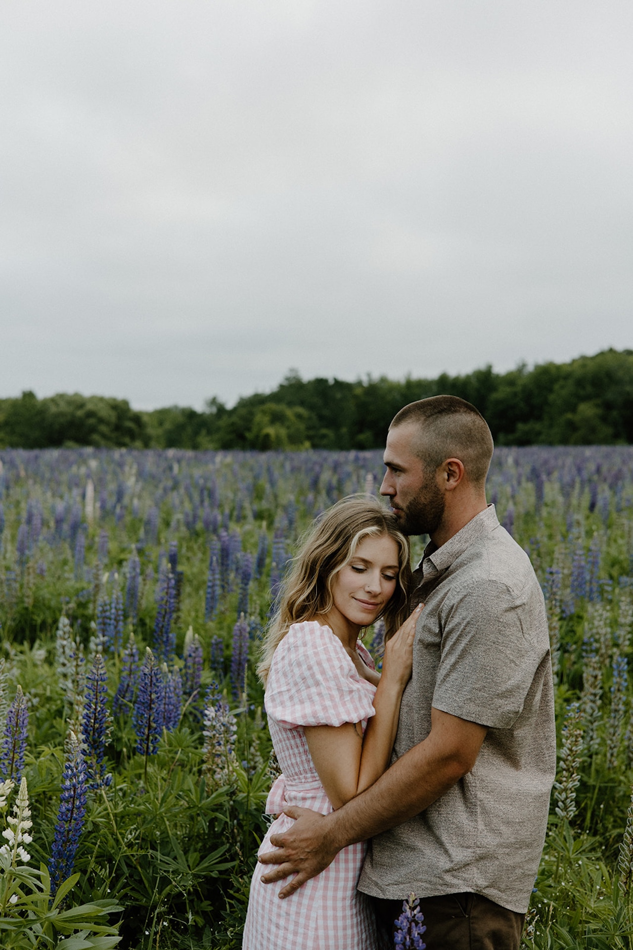 Couple standing close in a field of purple lupines, wrapped in each other’s arms at one of Maine’s most romantic Engagement Photo Locations.