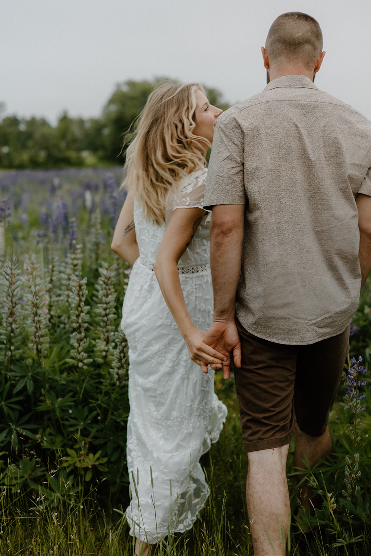 Couple walking through a field of Lupines, holding hands and smiling in a peaceful outdoor setting at one of Maine’s scenic Engagement Photo Locations.