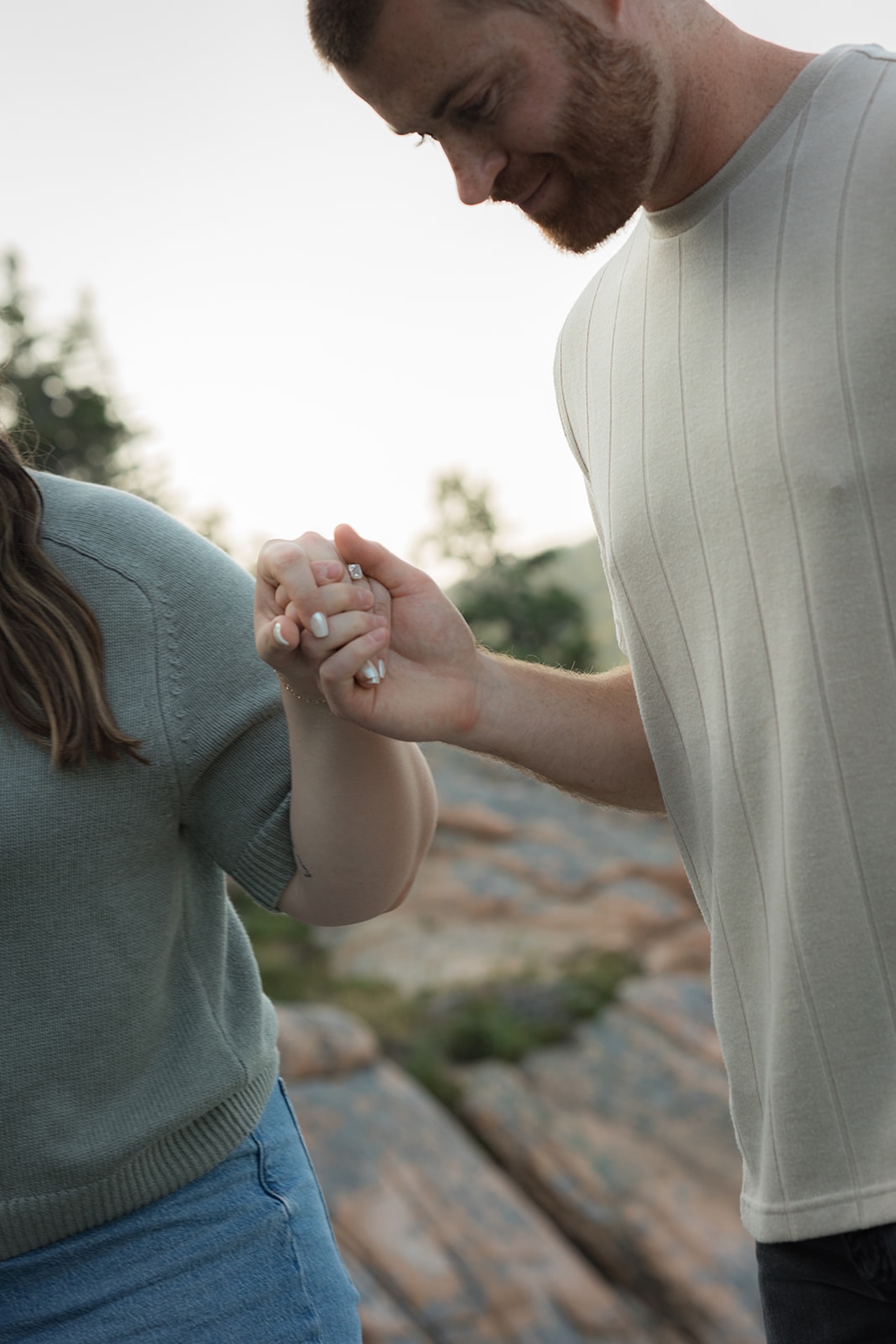 A close, intimate detail shot of a couple holding hands while walking across rocky ground, showing their rings and soft smiles.