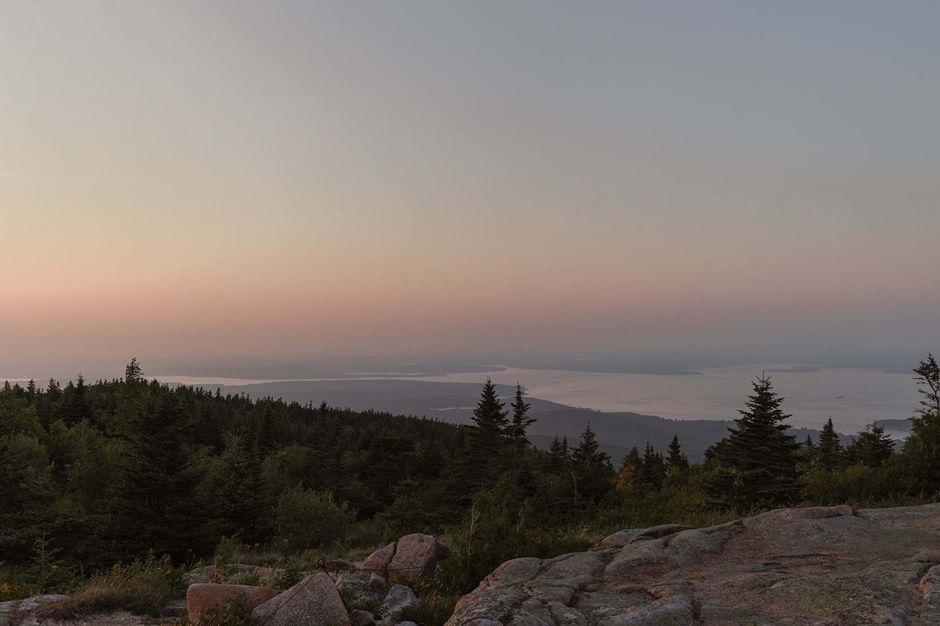 A scenic landscape overlooking Acadia’s coastline at dusk, with soft pastel skies and distant islands stretching across the horizon.