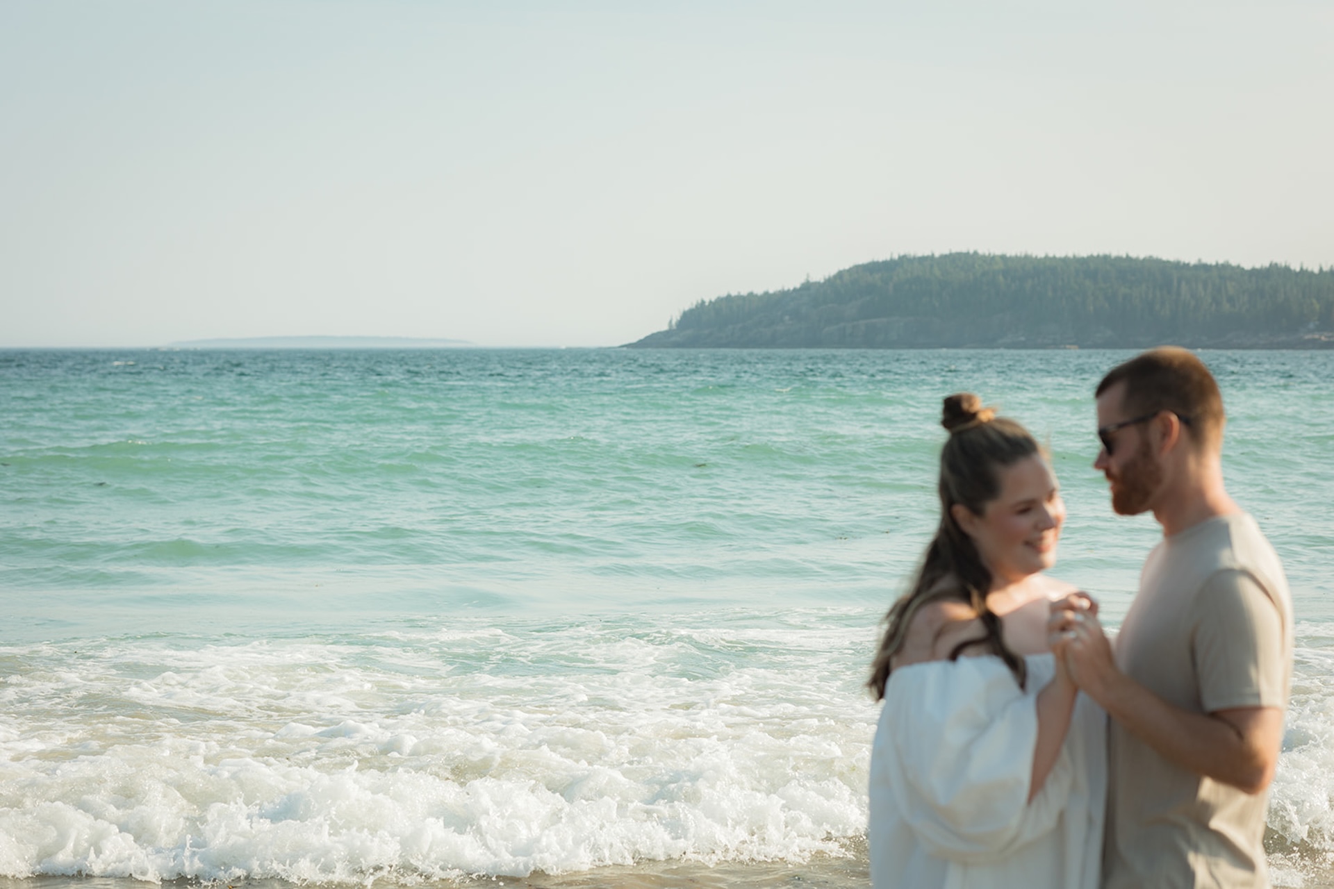 The couple dancing playfully at the shoreline with waves rolling in behind them, capturing a carefree moment from their Acadia engagement photos.