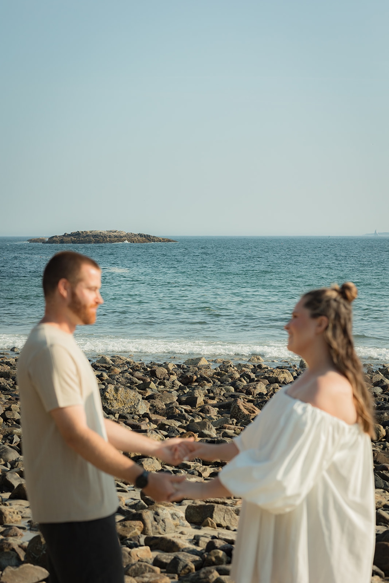 The couple dancing on the rocky beach with waves rolling in behind them, capturing a carefree moment from their Acadia engagement photos.