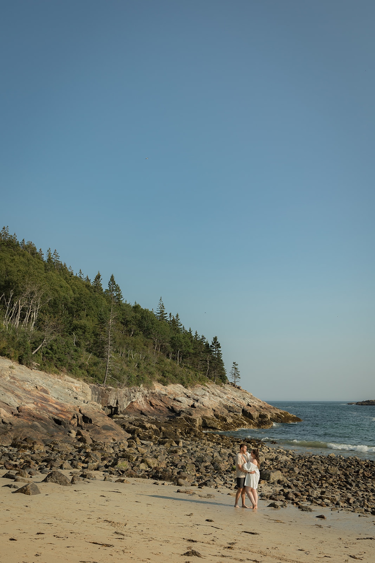 A couple walking along the beach at Acadia National Park during their Acadia engagement photo shoot