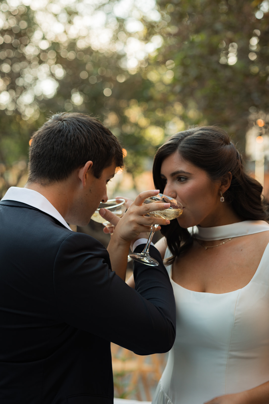 Bride and groom linking arms and sipping champagne together in the garden.