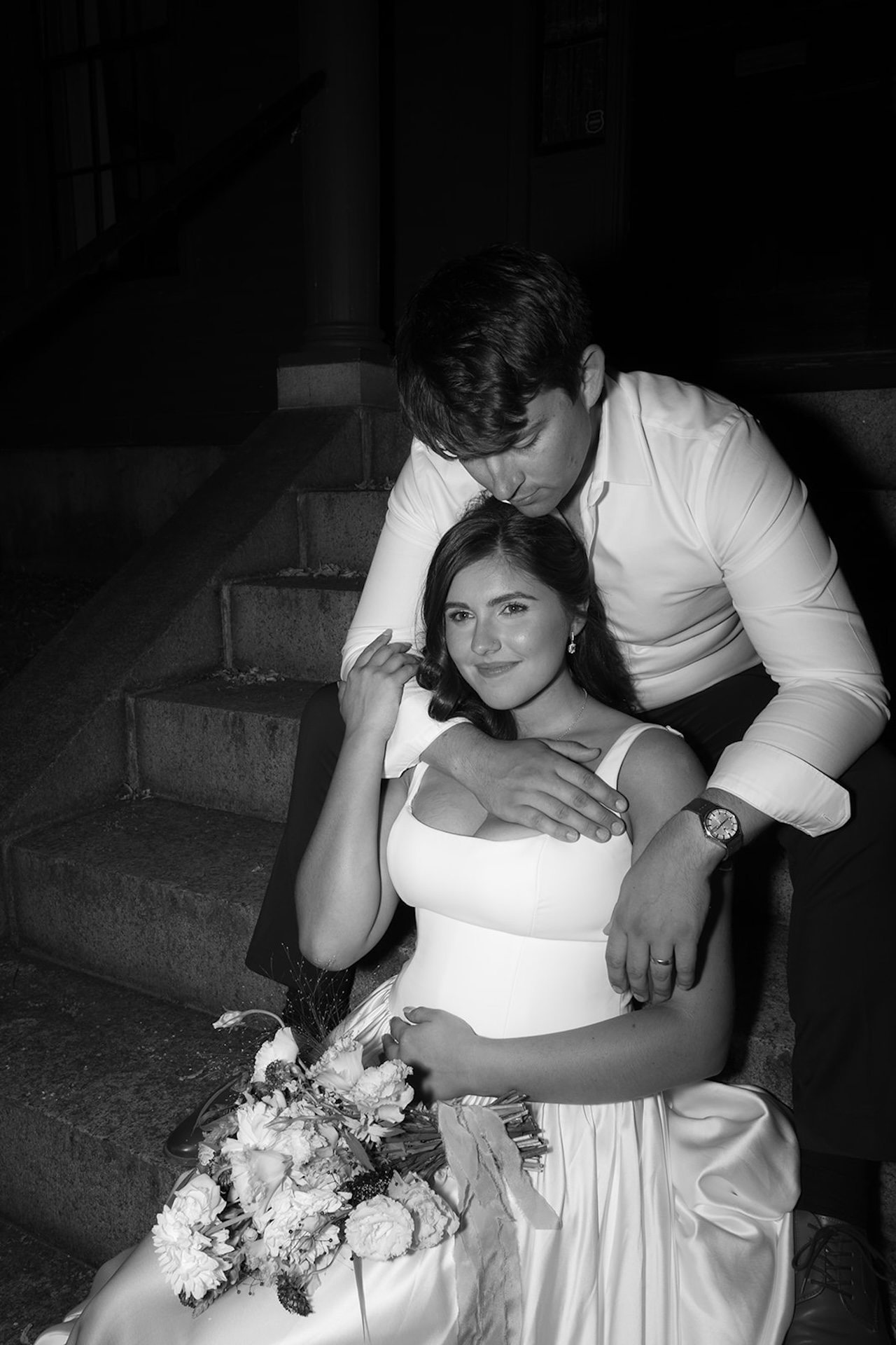 The couple sitting together on the stone steps, the groom holding the bride close.