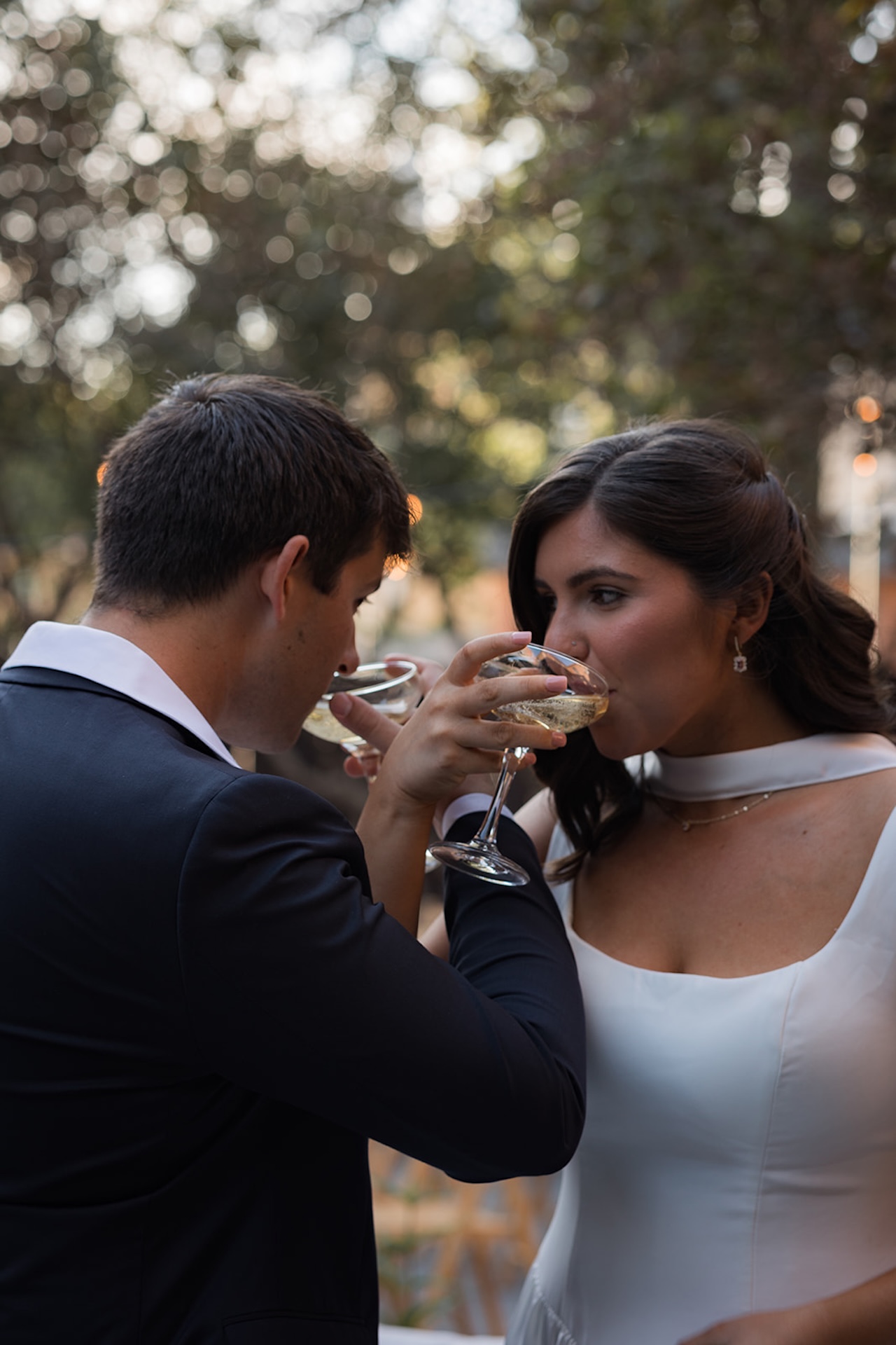 Bride and groom linking arms and sipping champagne together in the garden.