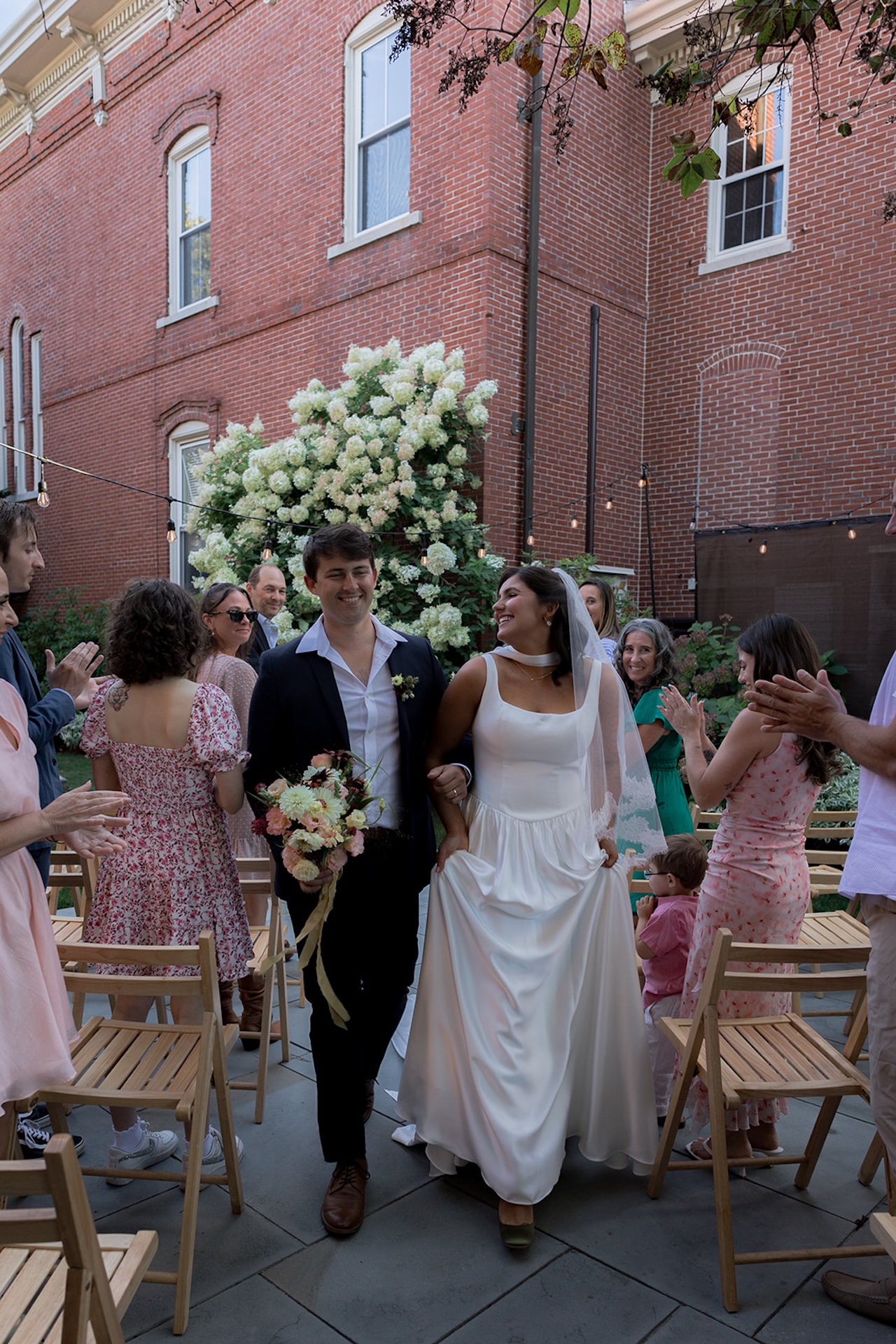 The newlyweds walk up the aisle smiling at each other as friends and family cheer.
